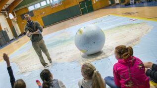 instructor teaching children in gym with giant map
