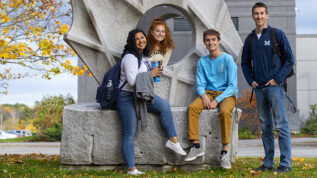 four students in front of sculpture on UMaine campus