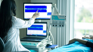 medical professional back to pointing at monitor as patient lays in bed