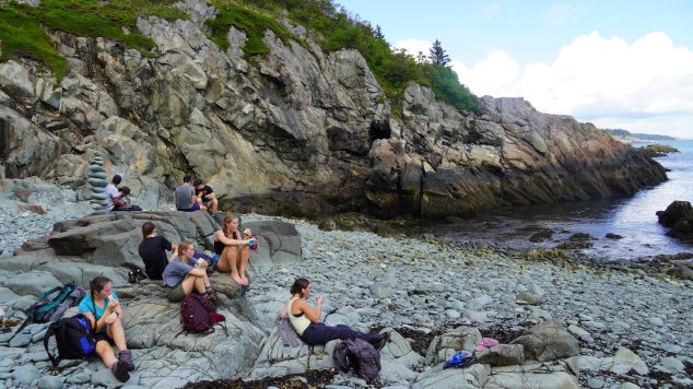 Students eat lunch sitting on rocky Maine beach