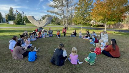 A group of children and app students sitting in a circle on a lawn.