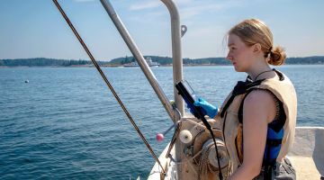 woman with blonde hair wearing a life vest takes environmental measurements off of a boat.