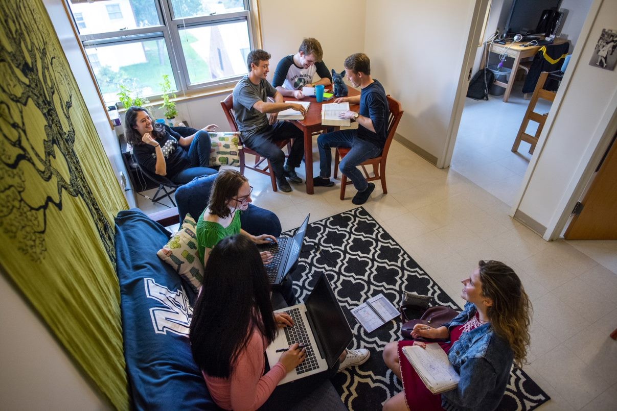 A group of students are gathered in a dorm room. 
