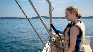 woman with blonde hair wearing a life vest takes environmental measurements off of a boat.